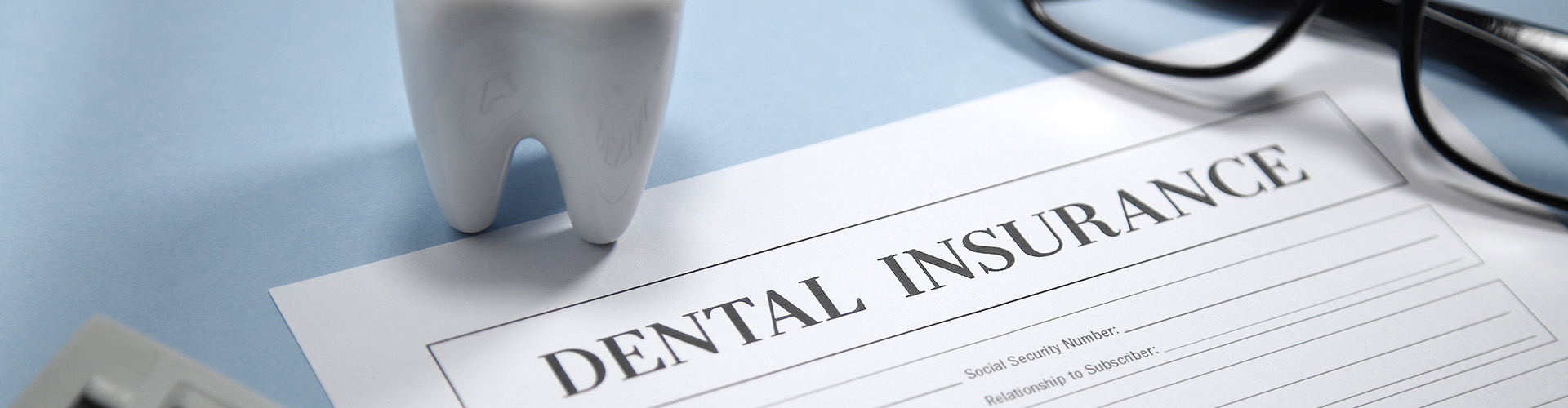 An image of dental insurance paperwork with a tooth figurine and a pair of glasses beside it.