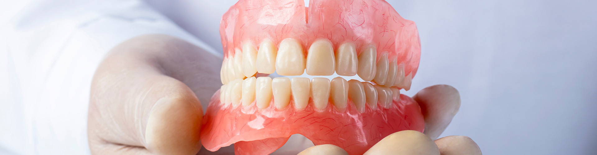 A denture being held by gloved hands.