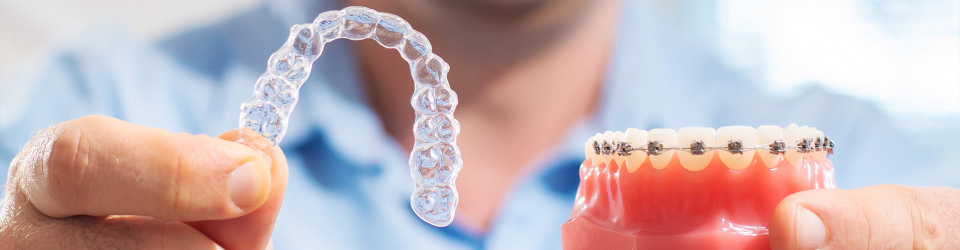 Smiling man holding clear aligner and braces model.