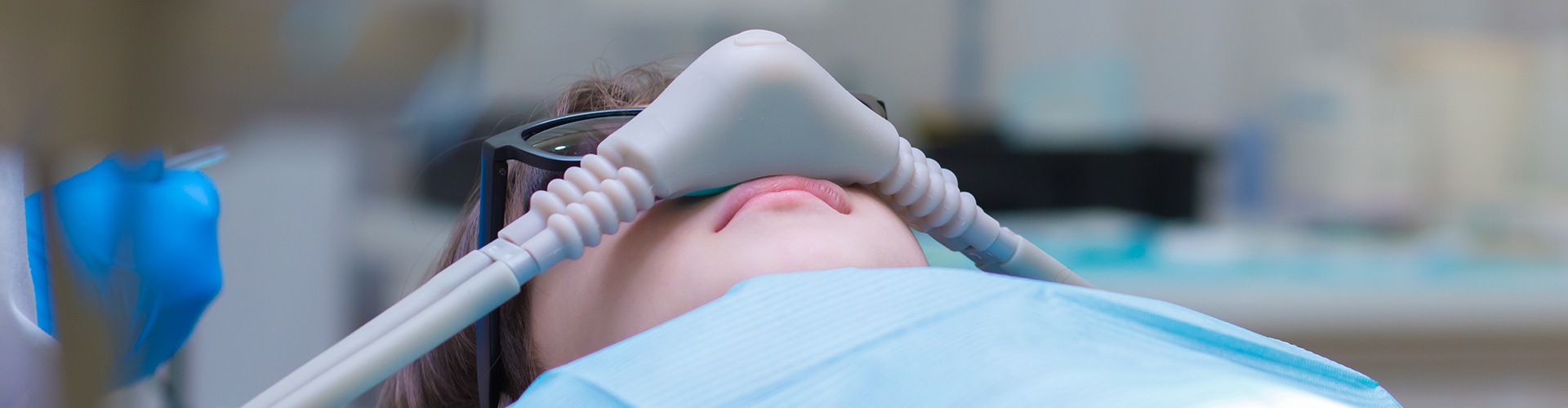 Person reclining in dental chair with a sedation mask on their nose.