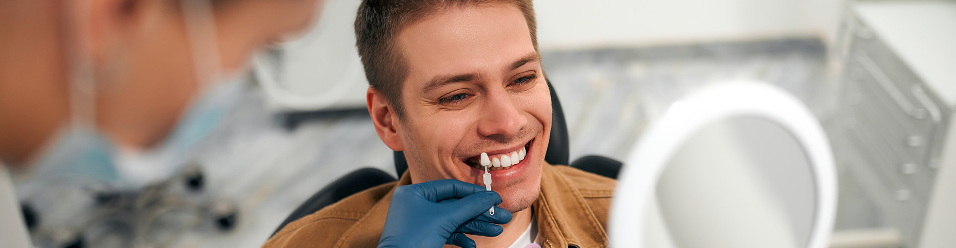 Dentist holding shade-matching tool next to patient's teeth.