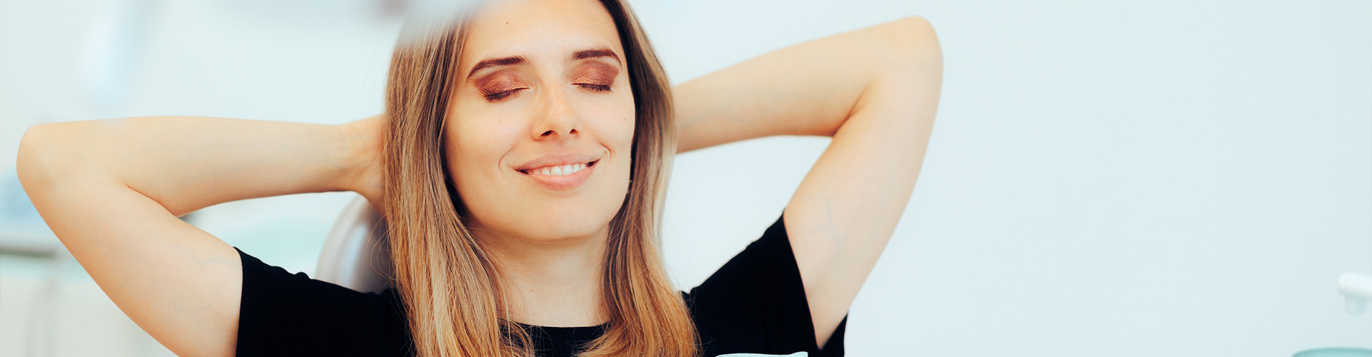Smiling woman relaxing in dental chair with hands behind her head.