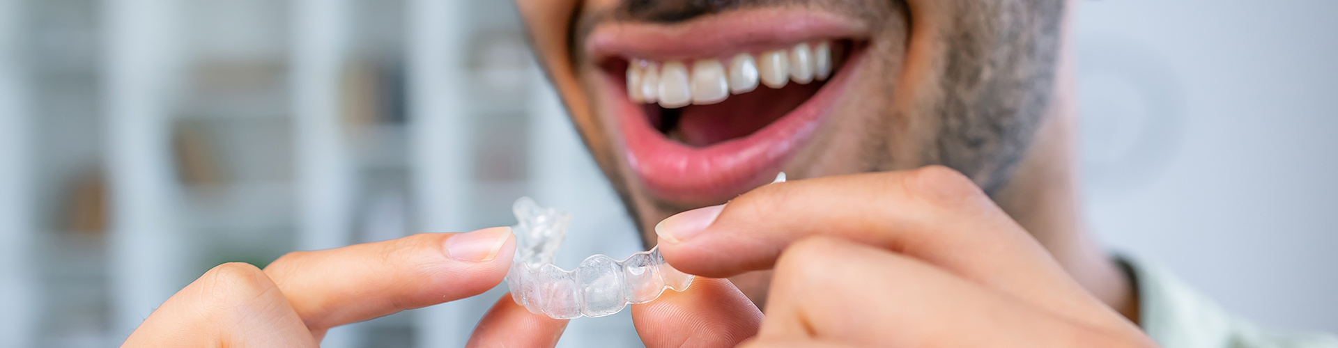 Smiling man holding clear aligner in front of his mouth.
