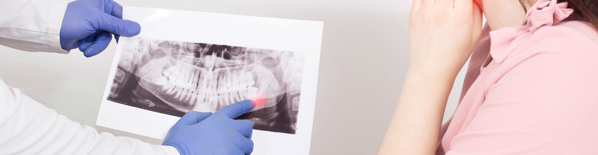 woman holding her jaw while doctor shows her an X-ray