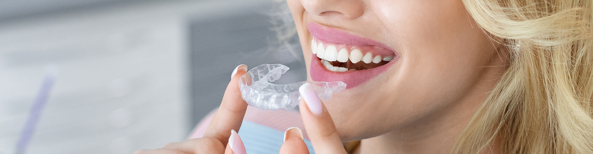 A woman smiling while inserting a clear aligner (Invisalign).