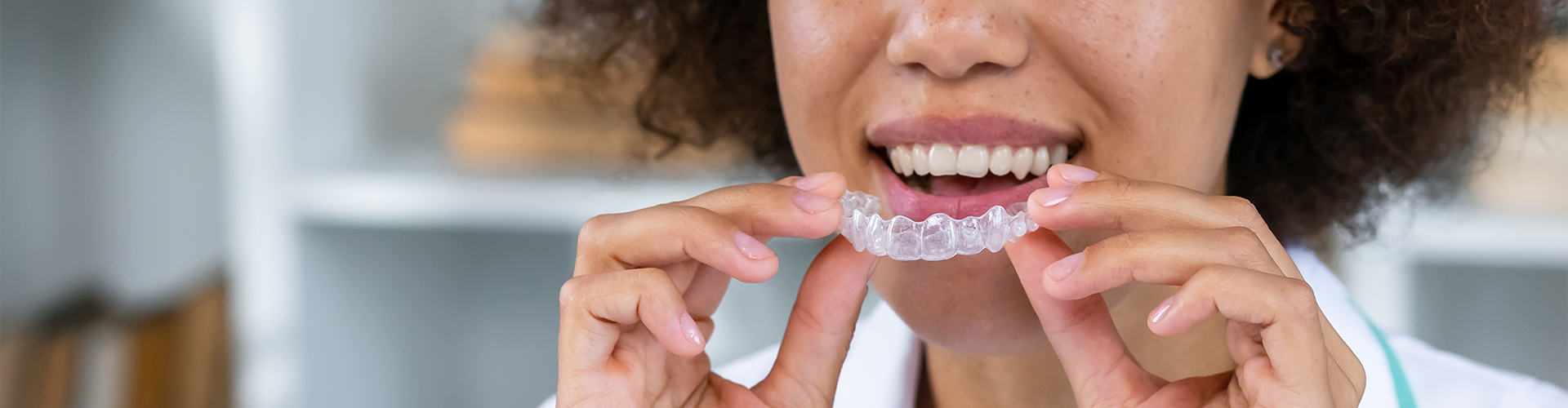 Smiling woman holding clear aligner.