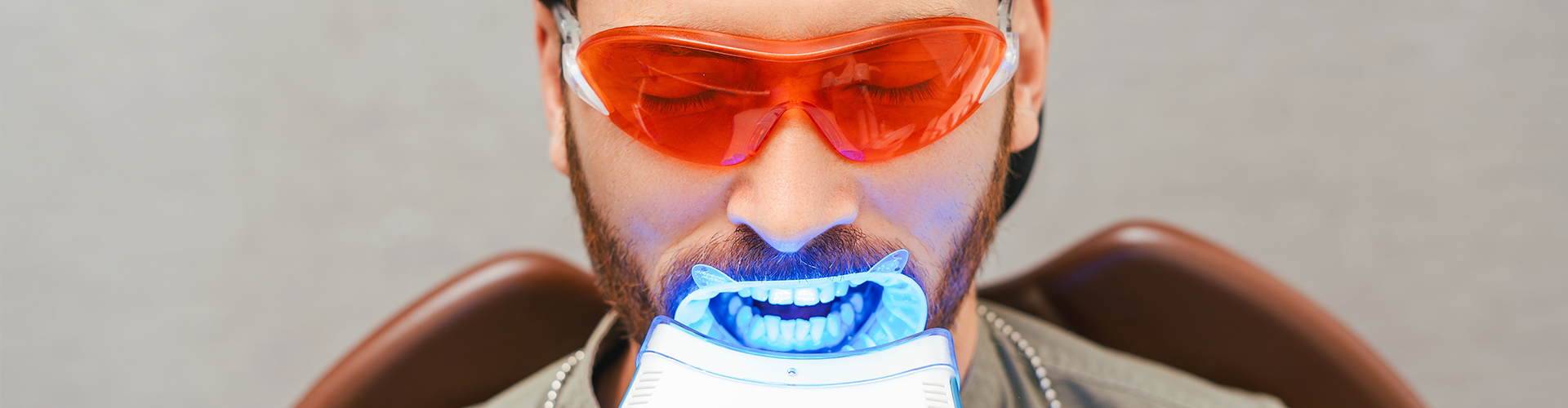 Led light shining in mouth of man wearing orange tinted glasses.