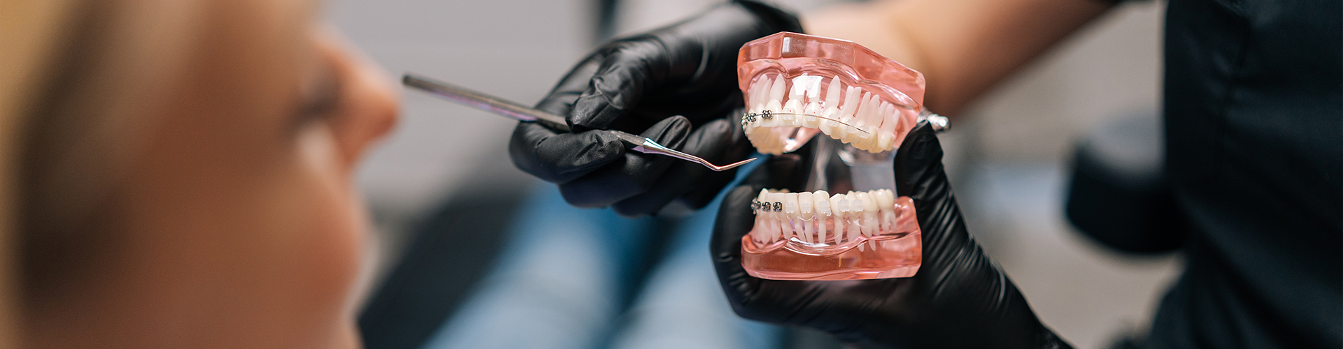 Gloved hands holding mouth model with braces in front of patient.