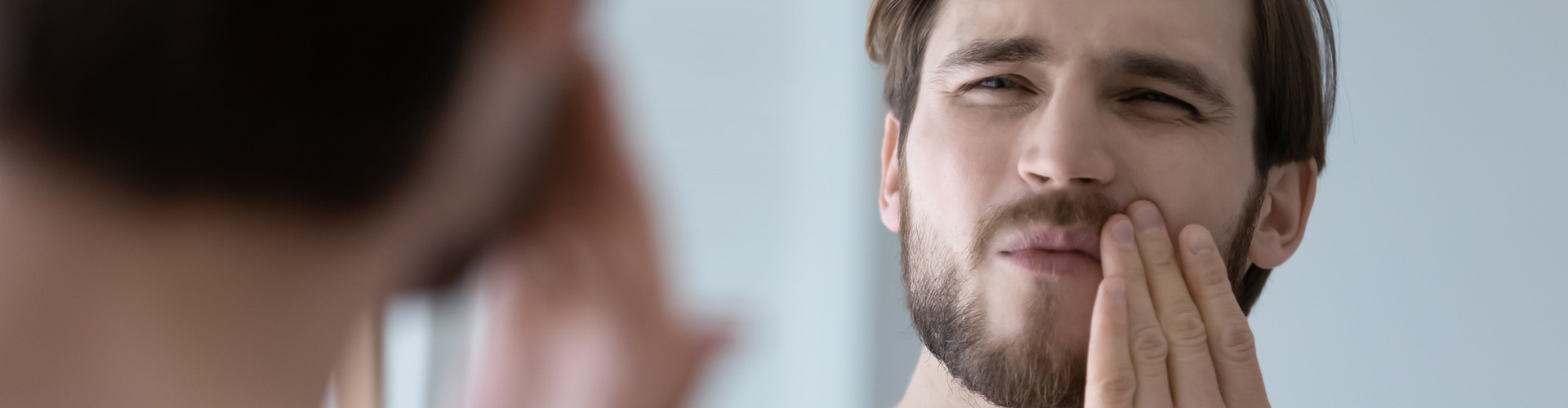 Man with toothbrush holding his mouth in pain.