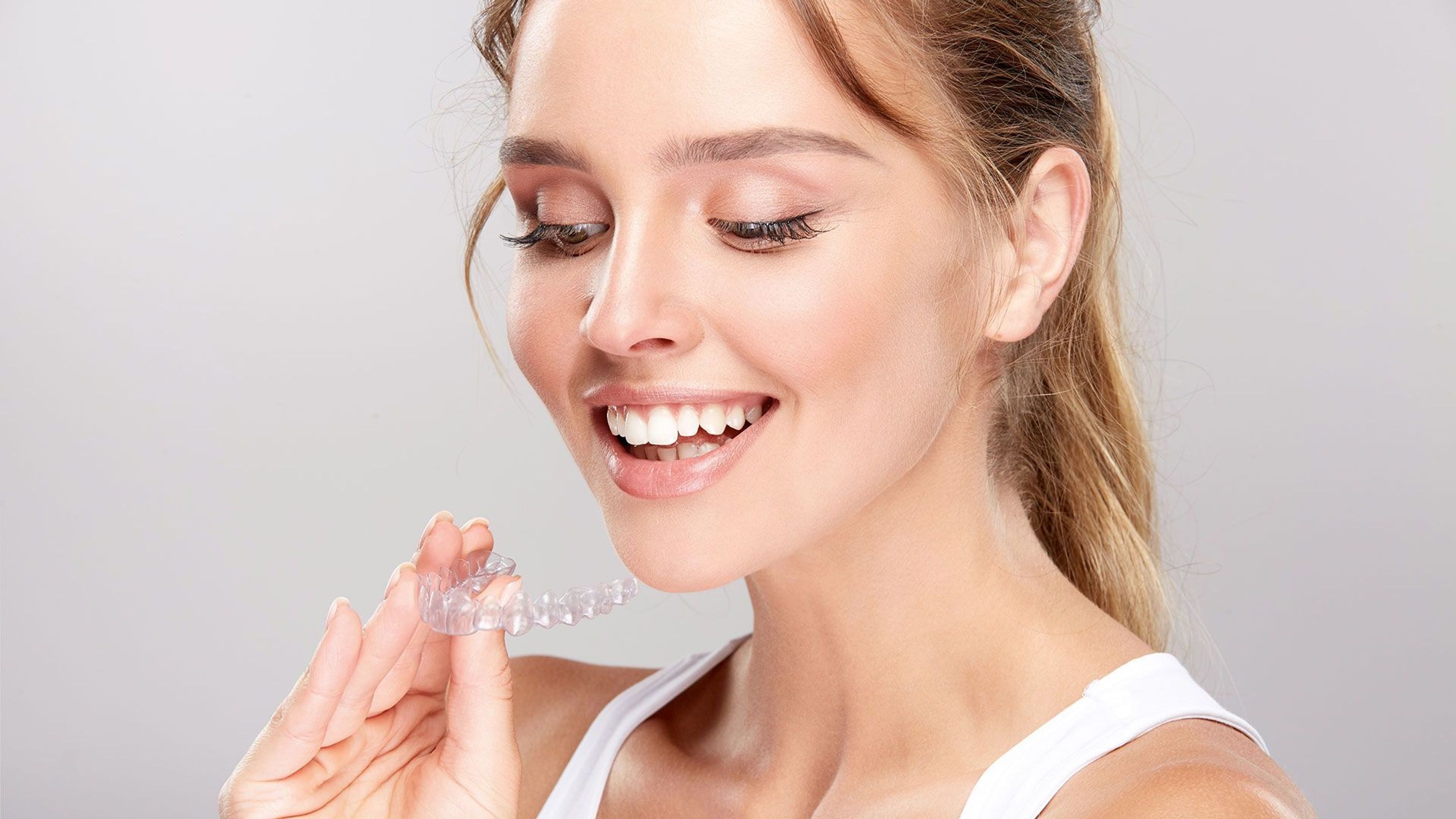 An image of a lady smiling and holding her Invisalign teeth aligners