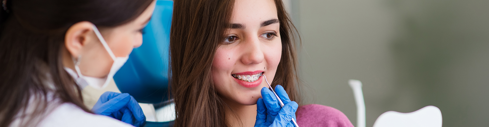 Girl with braces smiling while dentist holds dental tool at mouth.